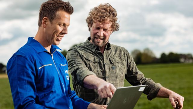 mannen buiten in veld wijzend naar laptop